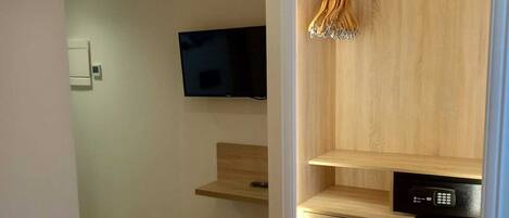 A bedroom with a bed, a TV, a wooden wardrobe, and a small chair.