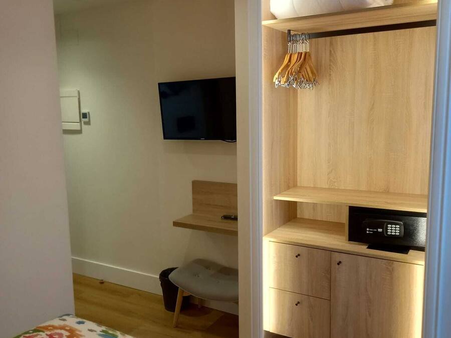 Een slaapkamer met een bed, een televisie, een houten kledingkast en een kleine stoel.