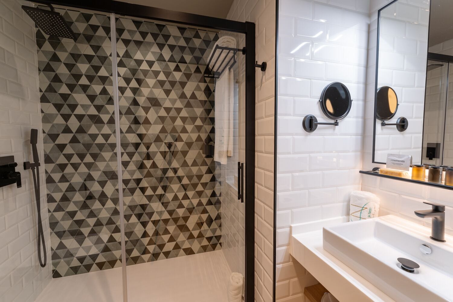 A modern bathroom with a geometric patterned shower enclosure, a white sink with a mirror, and a towel rack.