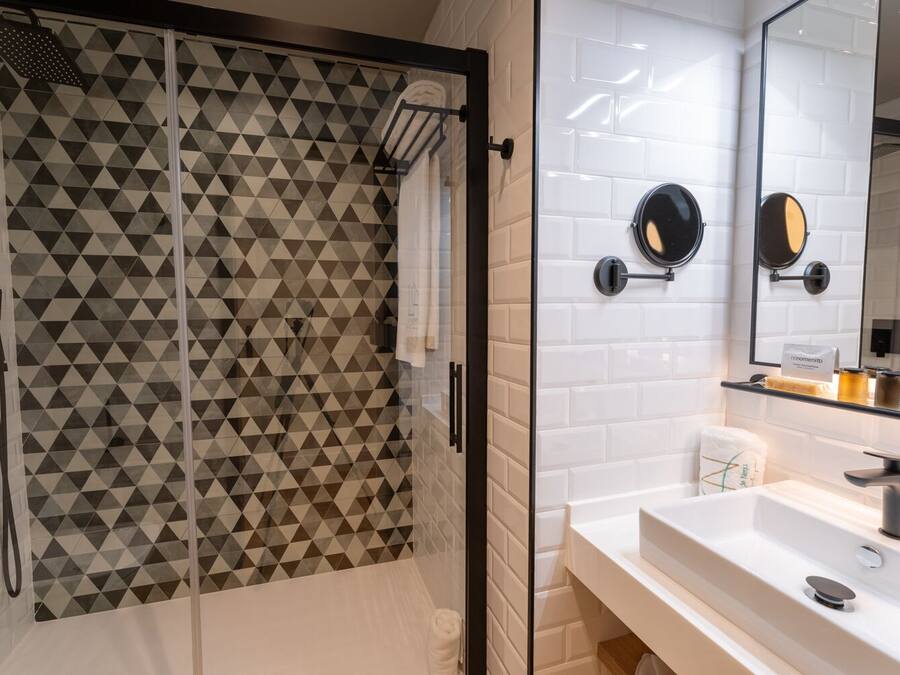 Un baño moderno con un box de ducha de diseño geométrico, un lavabo blanco con espejo y un perchero para toallas.