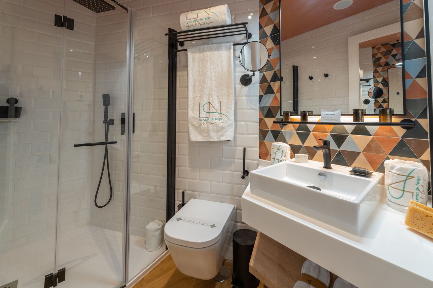 A modern bathroom with a glass shower enclosure, a white sink, and a mirror with a geometric tile backsplash.