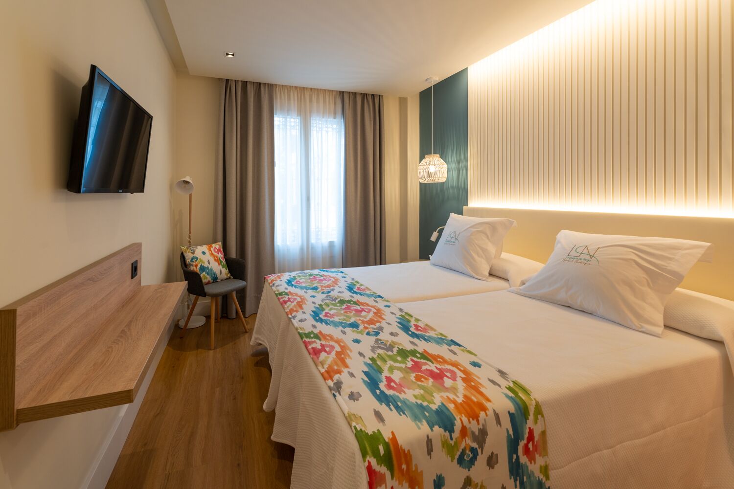 A hotel room with a bed, a desk, a chair, a TV, and a window with curtains.