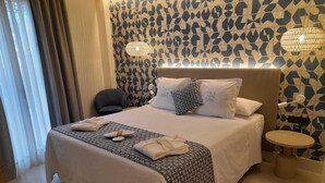 Habitación de hotel con una cama grande, una mesita de noche, una silla y un papel tapiz estampado.