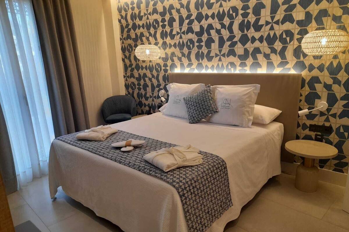 Habitació d'hotel amb un llit gran, una taula de nit, una cadira i una paret amb un disseny decoratiu.