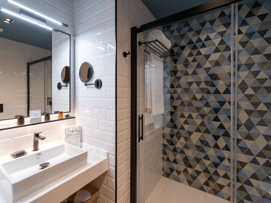 A modern bathroom with a white sink, two round mirrors, and a glass shower enclosure with geometric tile patterns.