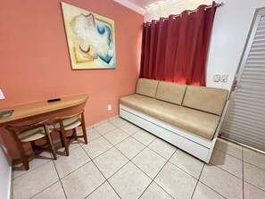 A room with a beige sofa, a wooden table with chairs, a painting on the wall, and a red curtain. - Diroma Fiori - JC TEMPORADA (Caldas Novas)