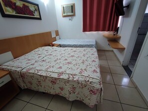 A bedroom with two beds, a wooden headboard, a wall-mounted air conditioner, a red curtain, and a small shelf with a lamp. - Diroma Fiori - JC TEMPORADA (Caldas Novas)
