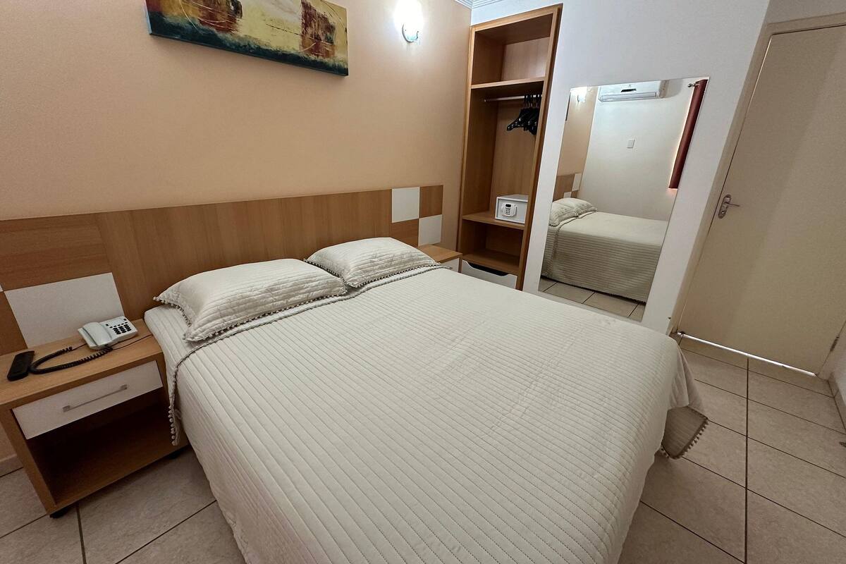 Une chambre d’hôtel avec un grand lit, une table de chevet avec un téléphone, une armoire et un miroir.