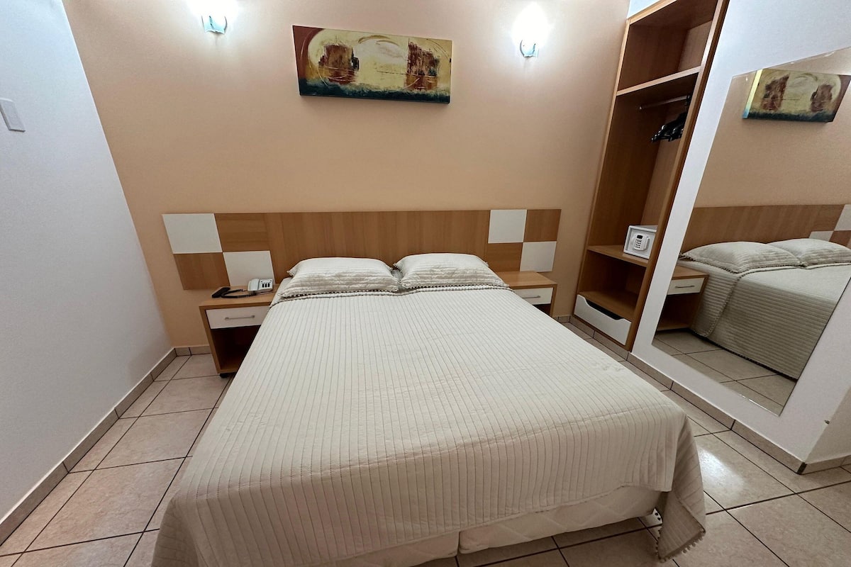 Une chambre à coucher bien rangée, avec un grand lit, des tables de chevet, une armoire et un tableau accroché au mur.
