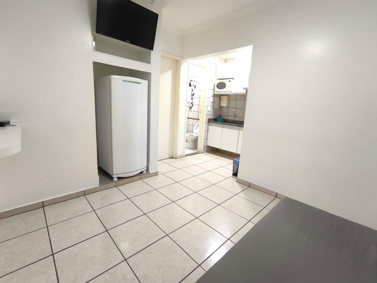 Um corredor com piso ladrilhado que leva a uma área de cozinha com geladeira e armários.