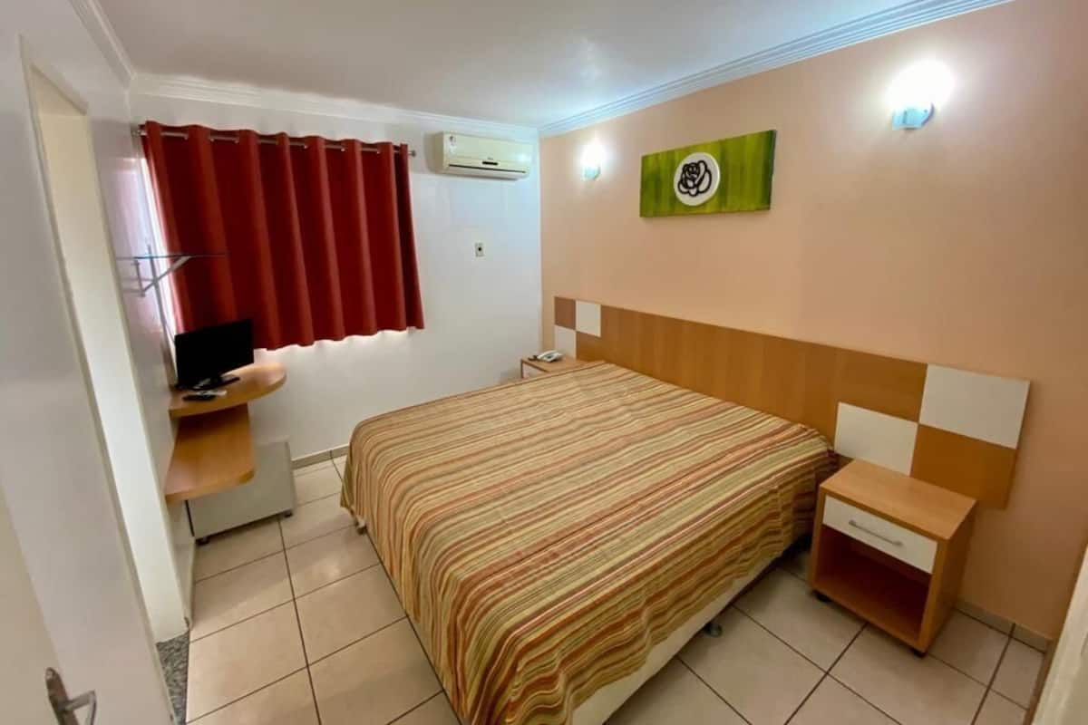 Une chambre d’hôtel équipée d’un lit, d’une télévision, d’un bureau et d’un climatiseur fixé au mur.