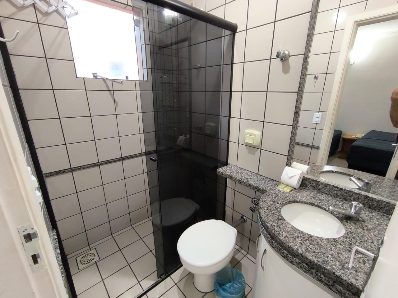 Casa de banho com chuveiro em cabine de vidro, sanita branca e lavatório com bancada de granito.