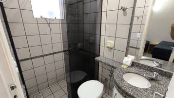 Casa de banho com chuveiro em cabine de vidro, sanita branca e lavatório com bancada de granito.