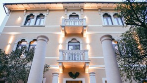 A building with a symmetrical facade, featuring a central balcony with a balustrade, flanked by columns, and multiple windows with shutters. - DeGrassi Boutique Garni Hotel Izola (Izola)