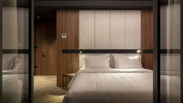 Una habitación de hotel moderna con una cama grande, un armario de madera y una mesita pequeña.