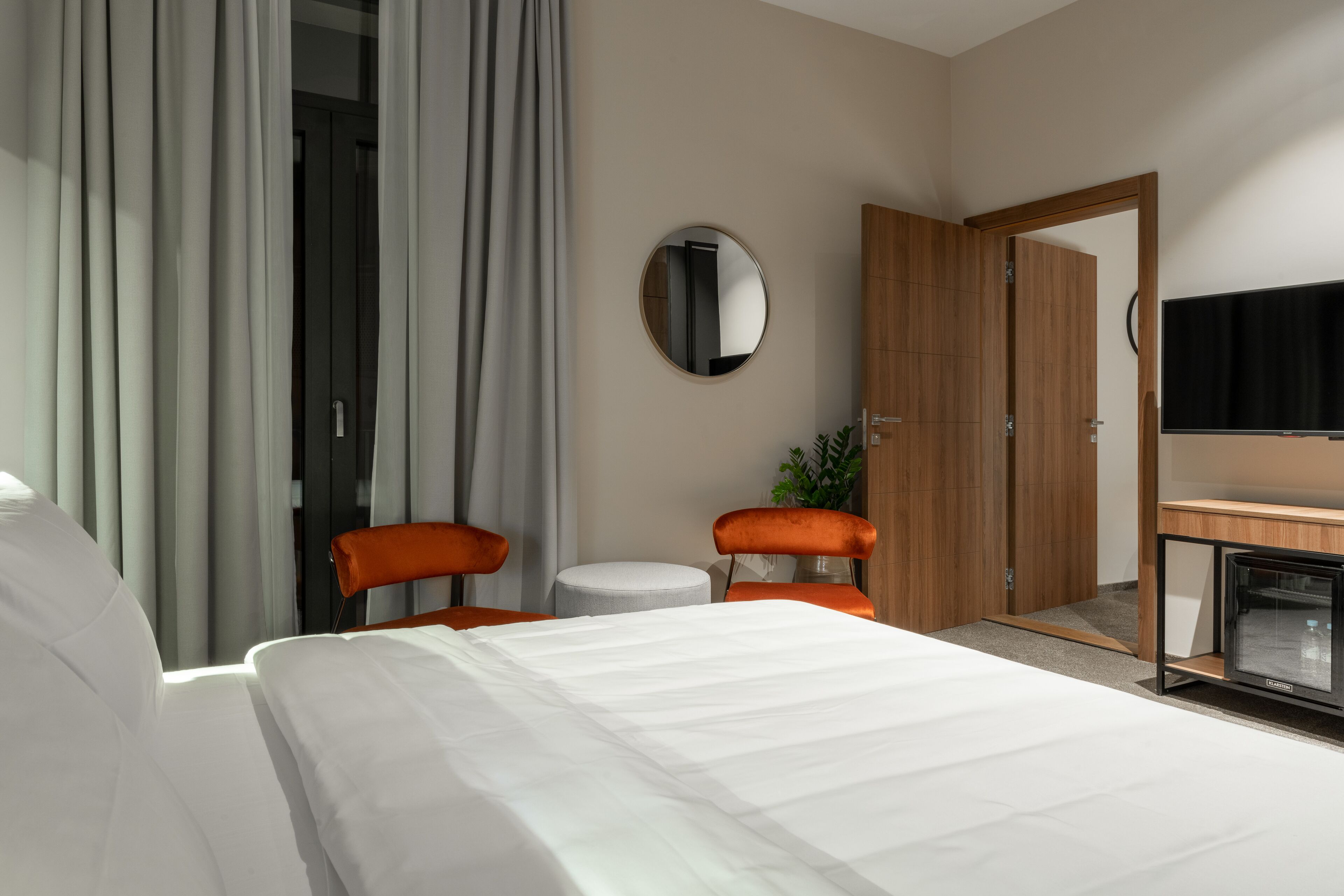 Ein Hotelzimmer mit einem Bett, zwei Stühlen, einem kleinen Tisch, einem Spiegel, einem Fernseher und einem Kleiderschrank.