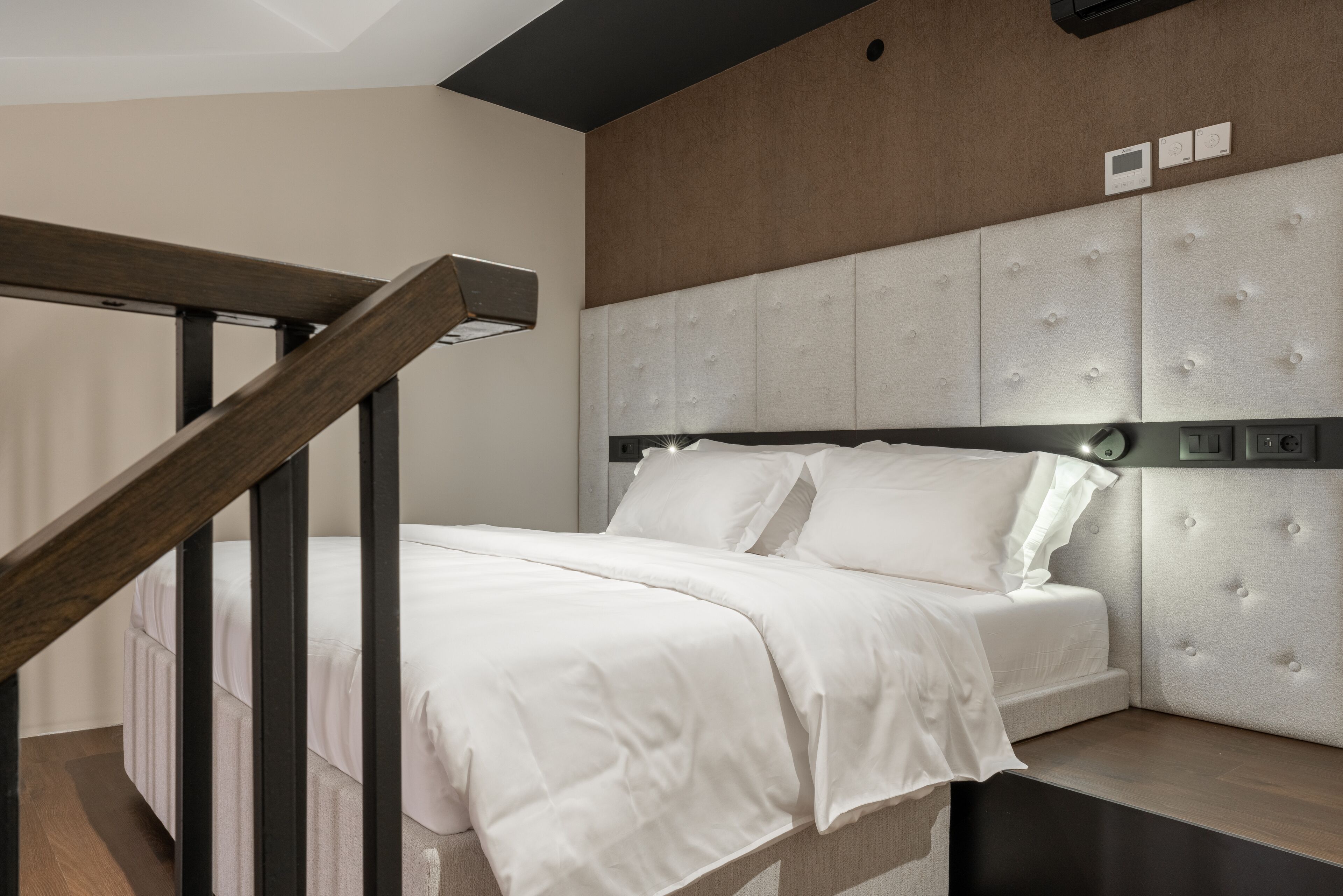 A modern bedroom with a wooden staircase, a tufted headboard, and a neutral color scheme.