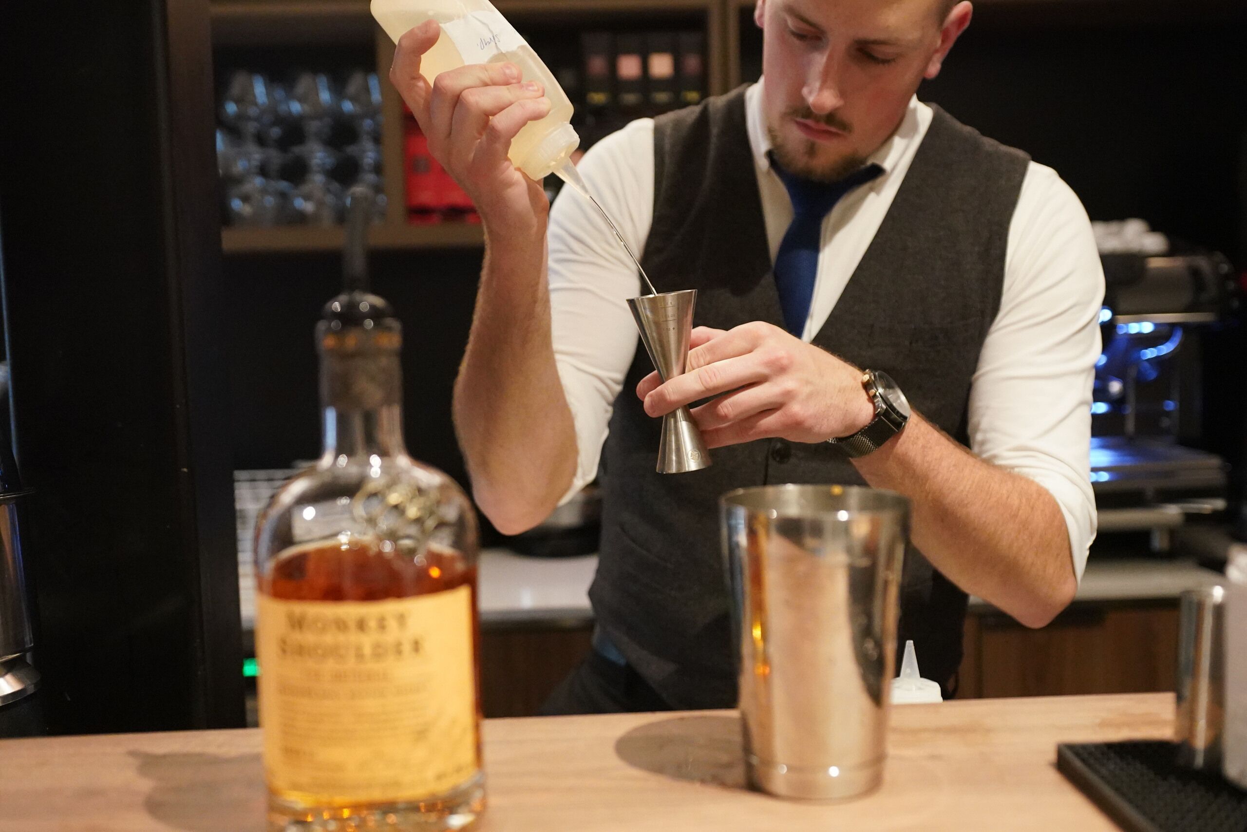 A bartender preparing a drink with a bottle of whiskey and a metal shaker.
