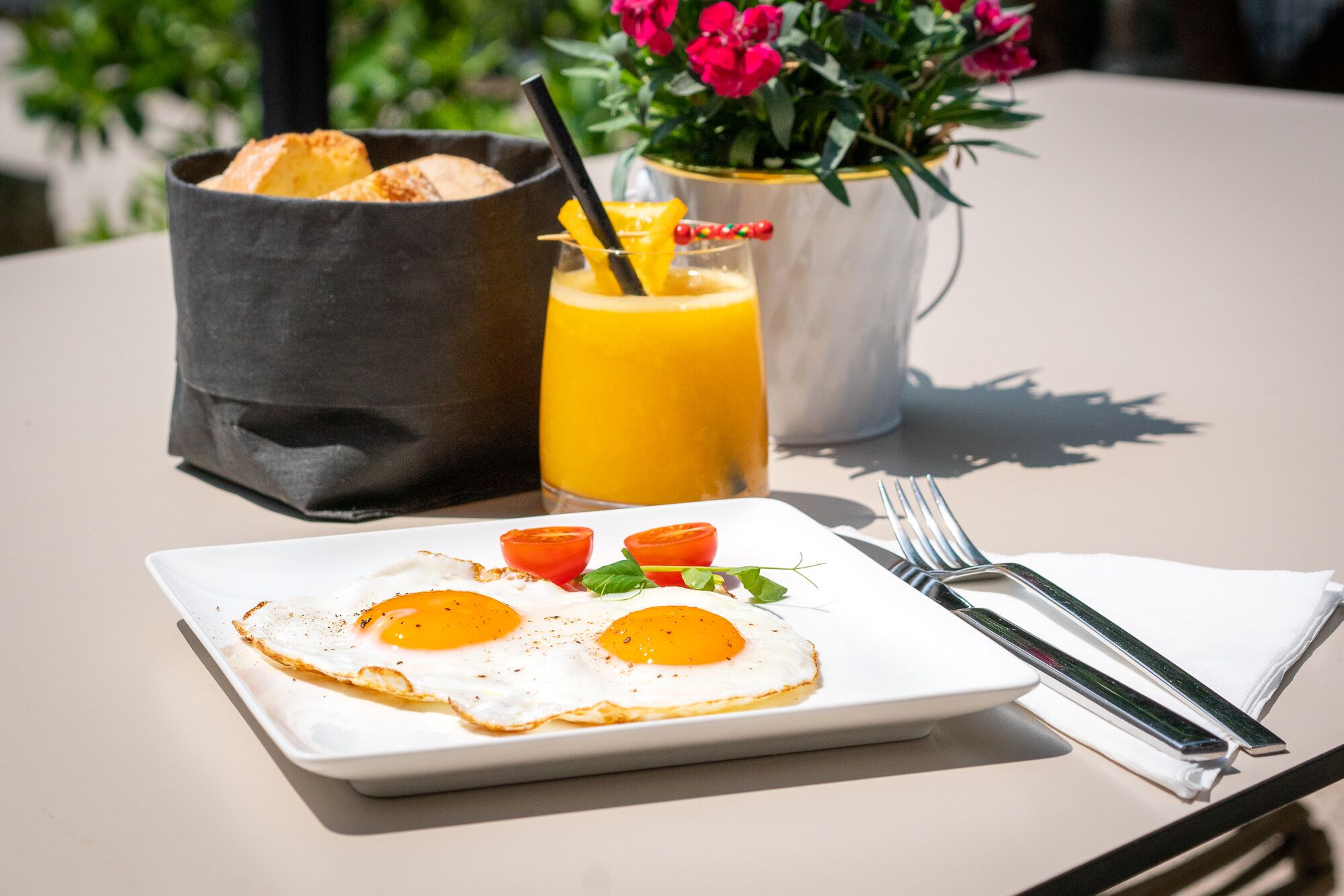 Un plato de desayuno con dos huevos fritos, una tostada y un vaso de jugo de naranja sobre una mesa.