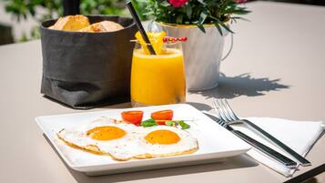 Un plato de desayuno con dos huevos fritos, una tostada y un vaso de jugo de naranja sobre una mesa.