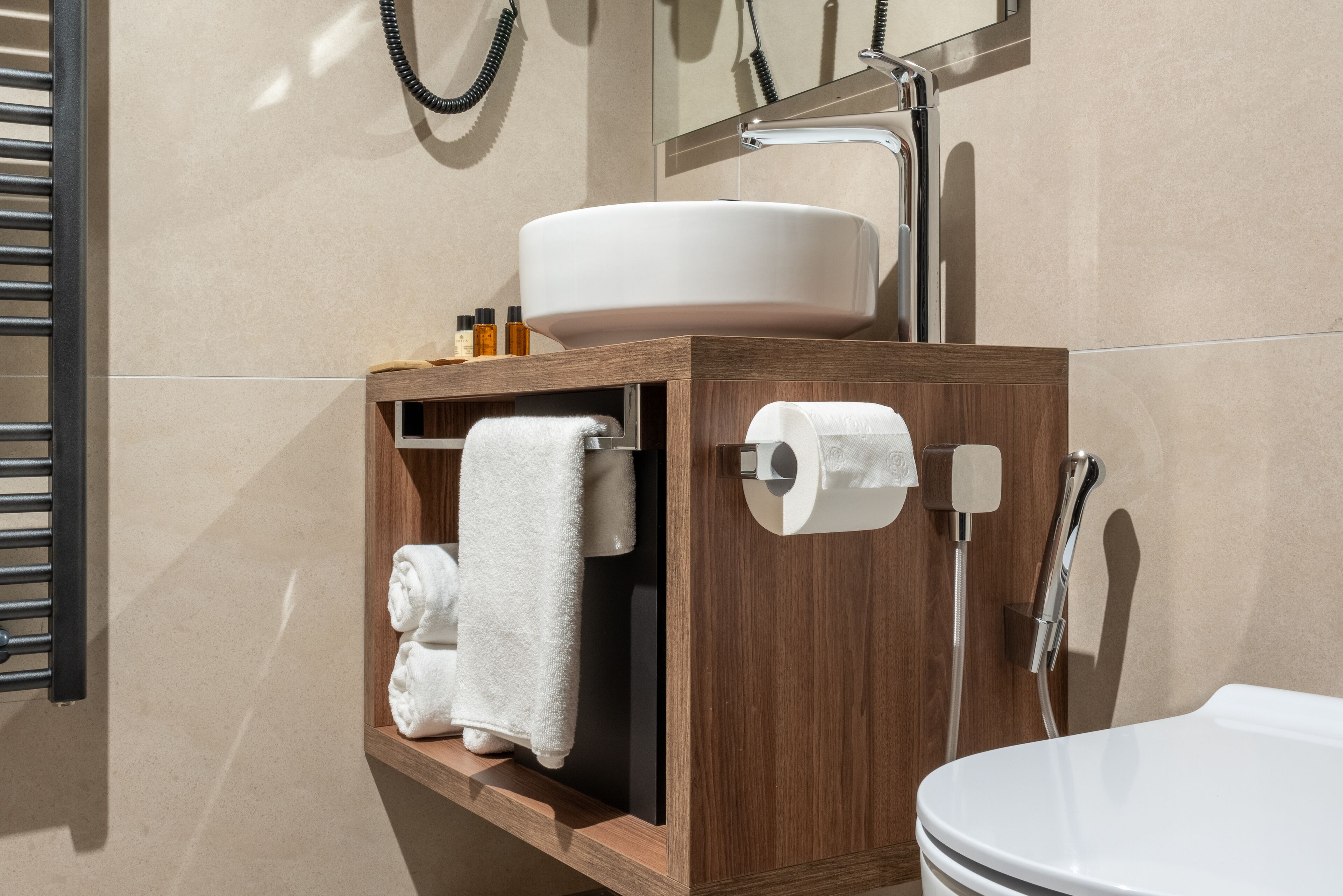 A bathroom with a wooden vanity, a white sink, a towel rack, and a toilet paper holder.