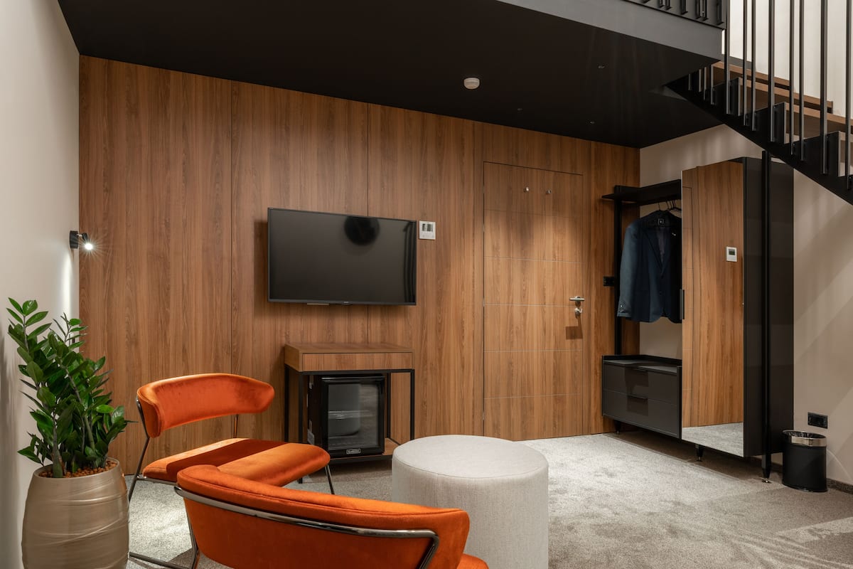 Quarto moderno com parede de madeira, TV de tela plana, uma TV pequena, um banquinho redondo, uma cadeira laranja e uma planta em vaso.