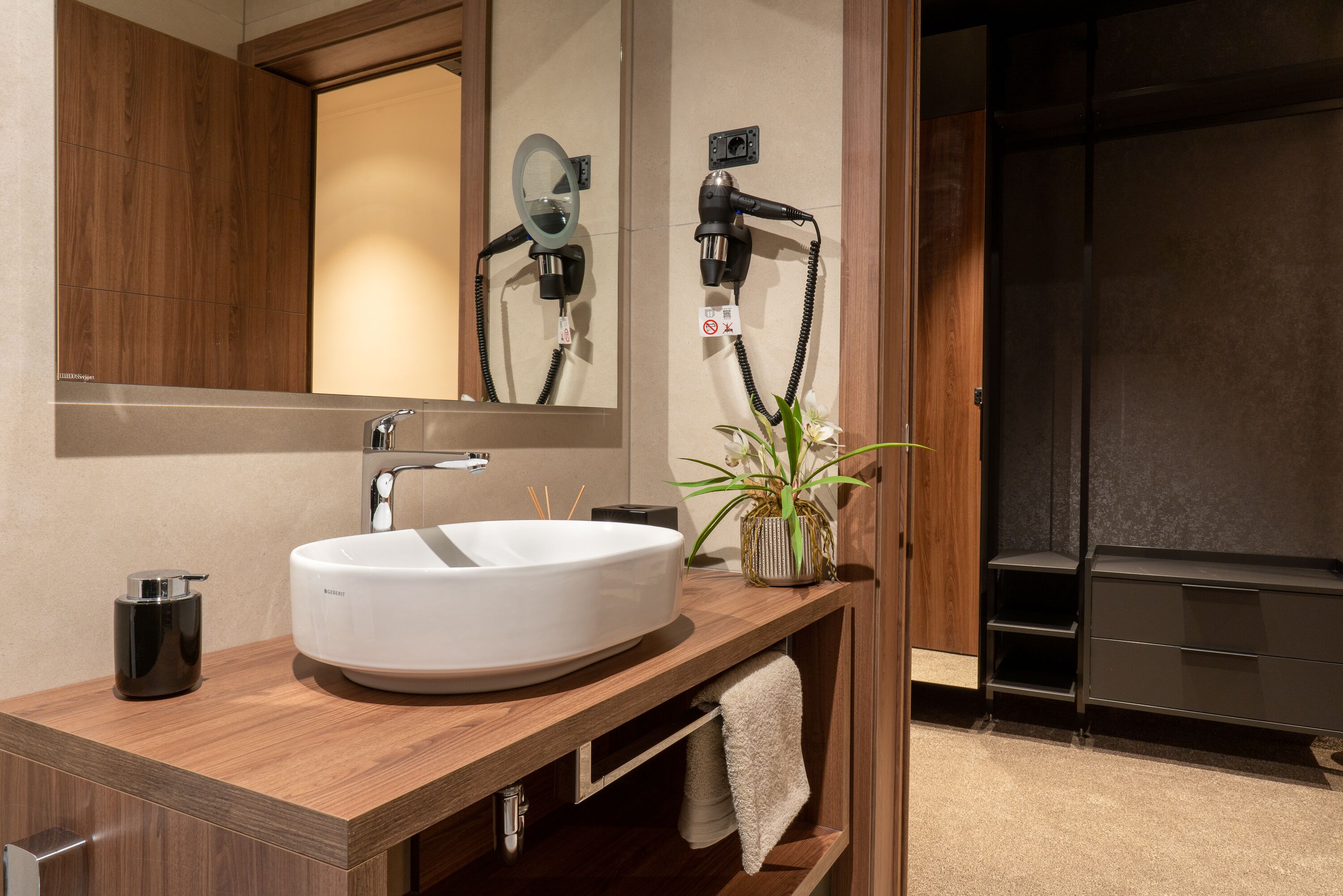 A modern bathroom with a large mirror, a white sink, a hairdryer, and a towel rack.