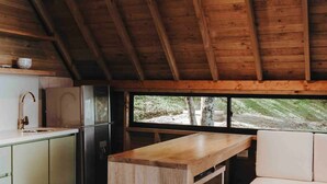 A rustic cabin interior with a wooden ceiling, a kitchenette with a sink and refrigerator, a wooden table, and a bench. - Cabaña Vacacional el Peñol con Jacuzzi (Guatapé)