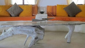 A room with a wooden table, a sofa with cushions, and a window with curtains. - Stunning 3-bed Villa in Watamu (Watamu)