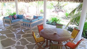 A covered outdoor seating area with a stone floor, a wooden table, and chairs with cushions. - Stunning 3-bed Villa in Watamu (Watamu)