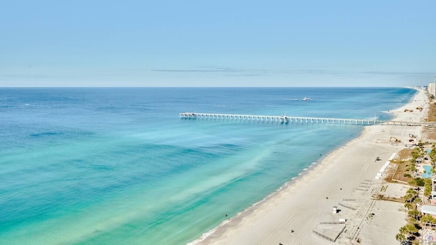 Een kuststrand met een lange pier die zich uitstrekt over de zee, een zandstrand en gebouwen langs de kustlijn.