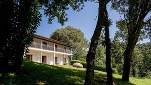 A two-story house with a balcony, surrounded by trees and a grassy lawn. - Hotel Rural Quinta de Novais (Arouca)