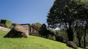 A house with a tiled roof, surrounded by a grassy hill and large rocks. - Hotel Rural Quinta de Novais (Arouca)