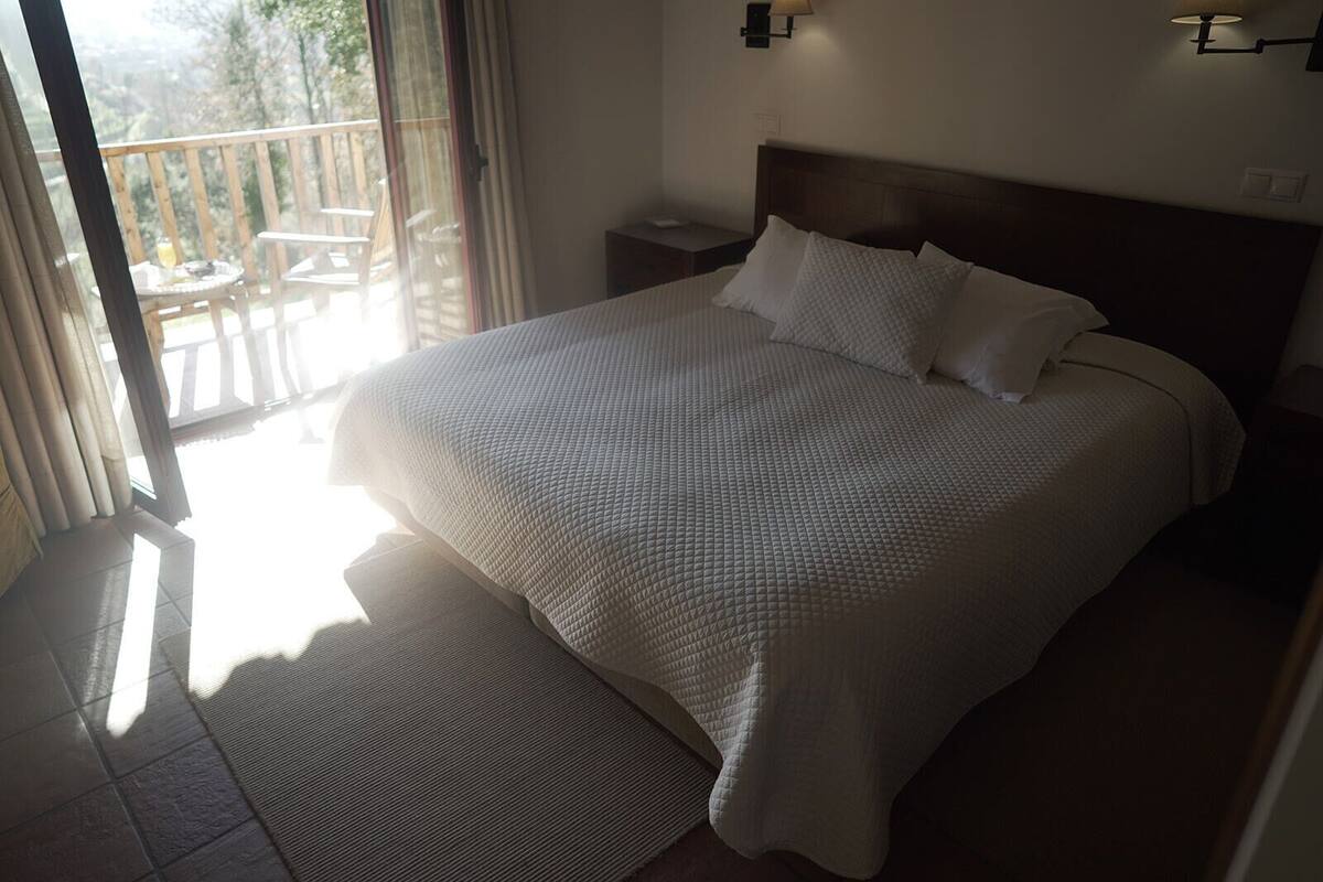 Un dormitorio con una cama grande, una mesita de noche, una lámpara y vistas al exterior.