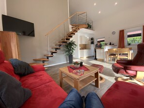 Una sala de estar moderna con un sofá rojo, una mesa de centro de madera y una escalera que sube a un nivel superior.
