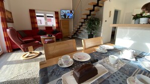 A modern living room with a red sofa, a wooden dining table set with plates, cups, and a chocolate cake, and a staircase leading to another level. - "Little uncle" (Wiefelstede)