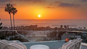 A sunset view from a balcony with chairs and a table, overlooking the ocean and a pier. - Oceanview Luxury Home - 5 Bedroom - 5 Baths - 3 Decks - Walk to Beach (San Diego)