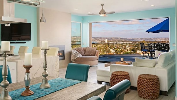 A modern living room with a large window, a ceiling fan, and a view of the cityscape. - Oceanview Luxury Home - 5 Bedroom - 5 Baths - 3 Decks - Walk to Beach (San Diego)