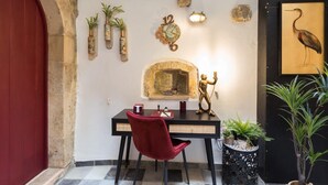 Un coin repas comprenant une chaise rouge, une table noire, une horloge murale, des plantes décoratives et une œuvre d’art encadrée.