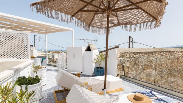 Une terrasse sur le toit, avec des meubles blancs, un grand parasol en osier et des plantes en pot.