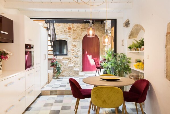 Una cocina moderna con pared de piedra, una puerta roja y una zona de comedor con dos sillas rojas y una amarilla.