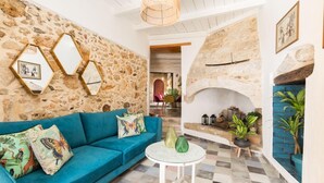 Un salon chaleureux avec un mur en pierre, un canapé bleu orné de coussins en forme de papillon, une table ronde blanche et une cheminée en pierre.
