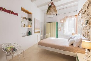 Un dormitorio con cama, una silla, estante con plantas y pared de piedra.
