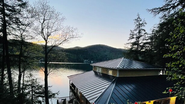 Un chalet au bord du lac, doté d’une terrasse et entouré d’arbres et de collines.