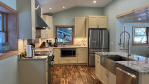 Une cuisine moderne avec un plancher en bois, des appareils électroménagers en acier inoxydable et une fenêtre donnant sur les arbres.