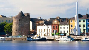 A waterfront with a historic tower, colorful buildings, and a sailboat. - Comeragh Pods (Comeragh)