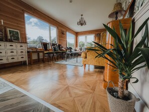 A spacious living room with wooden floors, a large window, and a dining area with chairs and a table.