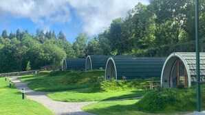 A row of green-roofed, semi-open structures with a gravel path leading to them. - Comeragh Pods (Comeragh)