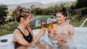 Two people in a hot tub with a scenic outdoor background. - Comeragh Pods (Comeragh)