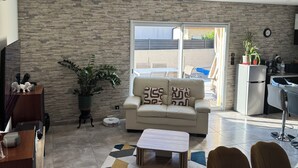 A modern living room with a sofa, coffee table, and dining area. A kitchen is visible in the background with a refrigerator and sink. - FULLY AIR-CONDITIONED, COMFORTABLE HOUSE WITH PRIVATE POOL (Sauvian)